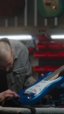Profesyonel erkek marangoz gitar tellerini bez parçasıyla siler ve gitarı detaylı bir şekilde inceler. Ahşap ustası, tasarımcı modern atölyede ahşap müzik aleti yapıyor. Dikey çekim