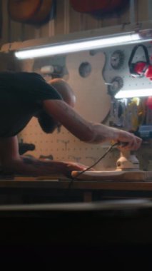 Erkek marangoz, ahşap gitar gövdesini cilalar, gitarın boynunu tamir eder. Ahşap ustası, zanaatkar modern atölyede müzik aleti yapıyor. Dikey çekim