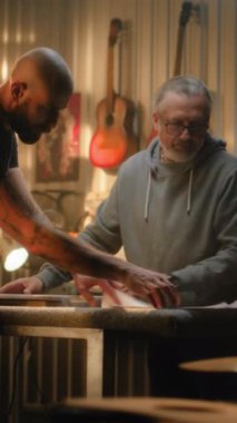 İki ahşap ustası, marangozlar çizimlere bakar, konuşur ve modern atölyede ahşap gitar yapımını, müzik aletlerini tartışırlar. Arka planda çalışan başka bir zanaatkar. El işi ve küçük işletmeler.