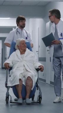 Doktor, kadın hasta klinik koridorunda yürürken tekerlekli sandalyeyi itiyor. Doktorlar yaşlı kadını ameliyata ya da ameliyathaneye götürürler. Hastane koridorunda tıbbi personel ve hasta var..