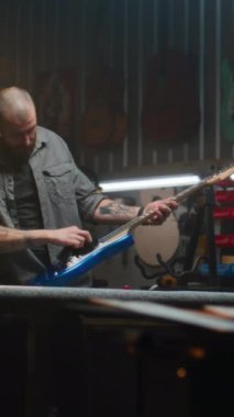Erkek marangoz gitar tellerini bez parçasıyla siliyor ve gitarı inceliyor. Ahşap ustası, tasarımcı modern atölyede ahşaptan müzik aleti yapıyor. El işi ve küçük işletme konsepti.