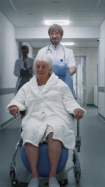 Genç doktor, tekerlekli sandalyedeki yaşlı kadın hastayı tıp merkezinin koridoruna naklediyor. Profesyonel sağlıkçılar tekerlekli sandalyedeki yaşlı kadınla konuşur. Sağlık uzmanı kapıyı anahtar kartıyla açıyor..