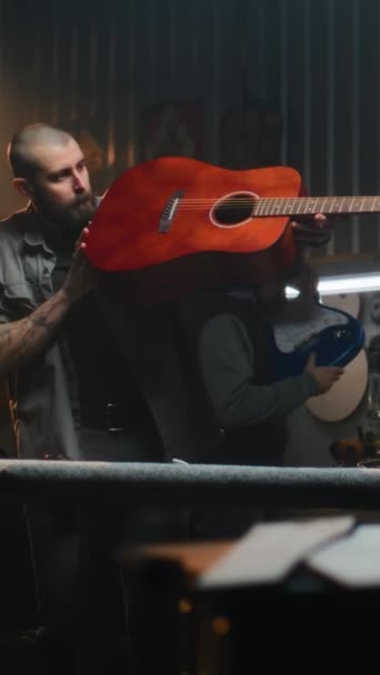 男工匠会弹奏吉他 检查声音 现代作坊的专业手工艺者用木料制作乐器 同事在后台工作 垂直射击 — 图库视频影像