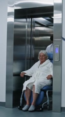 Doktor tekerlekli sandalyedeki hastayı asansörden çıkarıyor. Sağlık görevlileri yaşlı kadını prosedürlere ya da klinik koridorunda yürüyen ameliyathaneye götürüyor. Hastane koridorunda tıbbi personel ve hasta var..