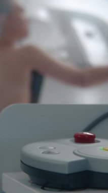 Yetişkin kadın, hastane radyoloji odasında mammografi taraması sırasında üstsüz duruyor. Radyolog kontrol panelindeki düğmeye basarak dijital mammografı çalıştırıyor. Modern klinik.