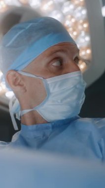 Laparoskopik aletler kullanarak ameliyat yapan profesyonel cerrahın yüzünü kapatın. Ameliyat lambası, ciddi şekilde yaralanmış hastalarla ameliyat masasını aydınlatıyor. Hastanede çalışan tıbbi personel..