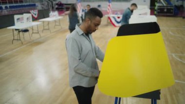 Amerika Birleşik Devletleri Başkanlık Seçimleri sırasında Afrikalı Amerikalı bir adam. Erkek ABD vatandaşı sandık merkezindeki oy verme kabininde duruyor ve düşünüyor. Vatandaşlık görevi ve vatanseverlik kavramı. Yüksek açı.