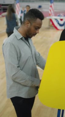 Amerika Birleşik Devletleri Başkanlık Seçimleri sırasında Afrikalı Amerikalı bir adam. Erkek ABD vatandaşı sandık merkezindeki oy verme kabininde duruyor ve düşünüyor. Vatandaşlık görevi ve vatanseverlik kavramı. Dikey