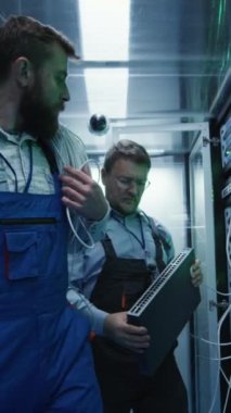Veri merkezi sunucu odasında çalışan iki erkek teknisyenin ağ ekipmanlarını tamir ve bakım için çıkarırken orta ölçekli bir fotoğrafı.