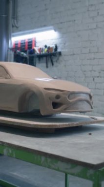 Çevre dostu bir otomobil prototipinin heykeli bir atölyedeki ahşap masaya yerleştirilmiş ve heykel aletleri yerleştirilmiş. Prototip bir arabanın tamamlanmamış heykeli. Dikey çekim.