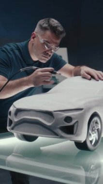 Otomotiv mühendisi bir araba prototipi heykelinin tasarım düzeltmelerini yapıyor. Değirmen makinesini kullanarak mükemmelleştiriyorum. LED 'li yüksek teknoloji laboratuvarı ve yeni bir araba modelinin taslakları. Dikey çekim