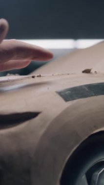 Erkek otomotiv tasarımcısının plasticine kilden çevre dostu araba modeli üzerinde çalışırken yakın plan çekimi. Yeni nesil elektrikli arabanın gelecekteki tasarımı. Modern araba tasarım stüdyosunda çalışıyorum. Dikey çekim.