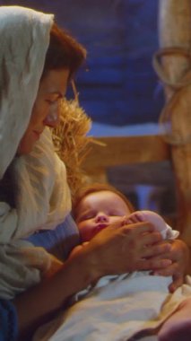 Joseph kuzuyu okşuyor ve Bethlehem 'deki loş bir ahırda uyuyan bebek İsa' yı kucaklıyor. Dikey çekim.