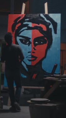 Karanlık atölyede çalışırken kadının yaratıcı portresine siyah boya süren tanınmamış bir adamın arka plan görüntüsü. Dikey çekim.