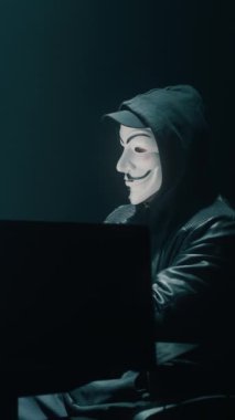Siyah kapüşonlu maskeli bir hacker büyük veri kurumsal sunucularına büyük bir veri saldırısı düzenlemek için bilgisayar kullanıyor. Bu sırada karanlık odada oturmuş veritabanını hackliyor. Dikey çekim.