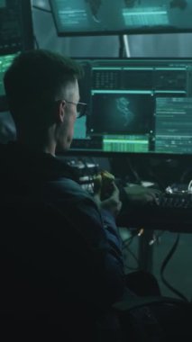 Genç adam donut yiyor, uzay gemisi ve uzay istasyonu bağlantılarını hackliyor geceleri karanlık odada masa başında otururken. NASA tarafından döşenmiş ekrandaki görüntüler. Dikey çekim.