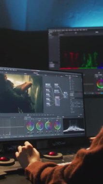 Editör stüdyoda bilgisayarda çalışıyor, renk derecelendirme kontrol paneli kullanıyor, video düzenliyor, film için renk düzeltmesi yapıyor. Program arayüzünü gösteren büyük ekranlar film görüntüleri, RGB grafikleri ve seviyeleri