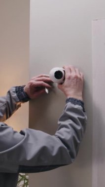 Üniformalı biri güvenlik kamerasını duvara yapıştırıyor ve sisteme kabloyla bağlıyor. Adam eve kamera yerleştiriyor. CCTV kameraları, izleme, güvenlik ve mahremiyet kavramı. Dikey çekim.