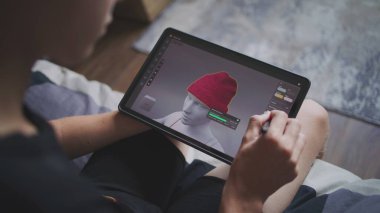 Elinde tablet olan ve dijital stili olan çocuk evde oturup 3 boyutlu modeller yaratıyor. Odaklanmış genç, 3D modelleme programı kullanarak oyun karakteri için kıyafet çiziyor. Geliştirme ve oyun tasarımı konsepti. Kapat..