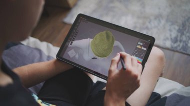 Elinde tablet olan ve dijital stili olan çocuk evde oturup 3 boyutlu modeller yaratıyor. Odaklanmış genç, 3D modelleme programı kullanarak oyun karakteri için kıyafet çiziyor. Geliştirme ve oyun tasarımı konsepti. Kapat..