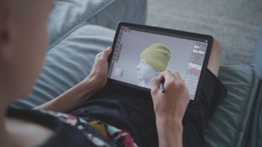 Elinde tablet ve dijital kalemle odaklanmış bir genç odada oturuyor ve 3D modeller çiziyor. Çocuk 3 boyutlu modelleme programı kullanarak yeni oyun karakterleri ve animasyonlar yaratıyor. Oyun tasarımı ve geliştirmesi. Kapat..