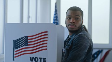 Afro-Amerikalı adam seçim merkezindeki oy verme kabininde duruyor ve karar veriyor. Birleşik Devletler 'de Ulusal Seçim Günü. ABD başkan adaylarının siyasi ırkları. Vatanseverlik ve vatandaşlık görevi.