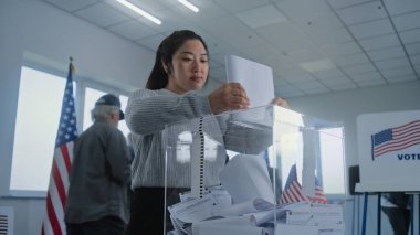 Asyalı genç kadın oy pusulasını kutuya koydu. Çeşitli Amerikan halkı ve ABD 'li seçmenler sandık merkezindeki oy kullanma kabinlerinde oy kullanıyor. Amerika Birleşik Devletleri 'nde seçim günü. Vatandaşlık görevi ve vatanseverlik kavramı