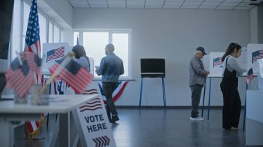 Afrikalı Amerikalı erkek kayıt masasındaki kadın oy pusulasından oy alır ve oy verme kabinine gider. Çok ırklı Amerikan vatandaşları sandık merkezinde oy kullanıyor. Birleşik Devletler Seçim Günü.