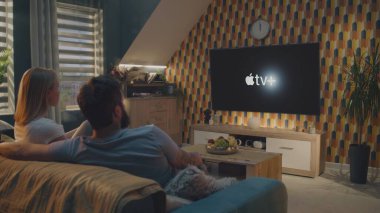 ZAPORIZHYA, UKRAINE - 7 Haziran 2024: Yetişkin Kafkasyalı çift konuşur ve Apple TV 'de film veya dizi izlemeye başlar kanepede oturur ve evde dinlenir. Apple TV logosu