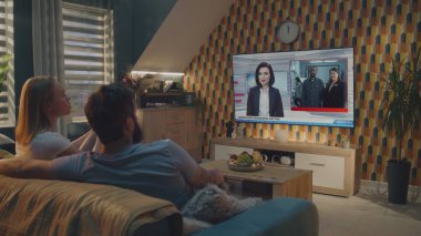 Beyaz çift büyük bir televizyon programında flaş haber izliyor ve evdeki koltukta otururken ABD başkanlık seçimlerini tartışıyor. TV 'de kadın haber spikeriyle televizyon haberleri yayınlanıyor
