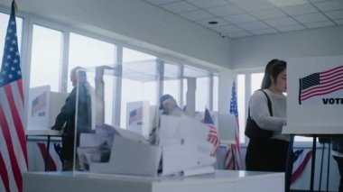 Asyalı kadın oy pusulasını kutuya koyar. Çok kültürlü Amerikan halkı ve ABD 'li seçmenler sandık merkezindeki oy kullanma kabinlerinde oy kullanıyor. Amerika Birleşik Devletleri Seçim Günü. Demokrasi ve vatanseverlik kavramı.
