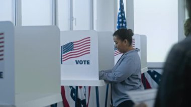 Çoklu etnik Amerikan vatandaşları oy kullanma merkezindeki kabinde oy kullanmaya geliyorlar. Birleşik Devletler 'de Ulusal Seçim Günü. Başkan adaylarının politik ırkları. Vatandaşlık görevi, vatanseverlik kavramı.