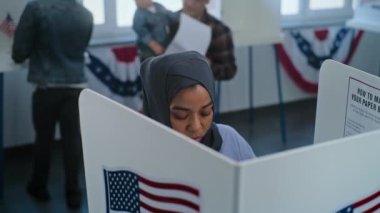 Tesettürlü Müslüman kadın oy verme merkezindeki oy kabininde duruyor. Birleşik Devletler 'de Ulusal Seçim Günü. ABD başkan adaylarının siyasi ırkları. Vatandaşlık görevi kavramı. Dolly vurdu..