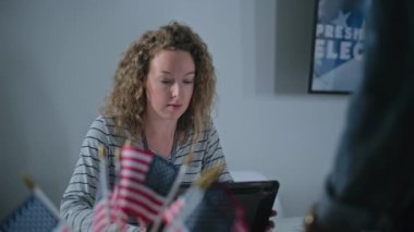 Kadın anket memuru Afrikalı Amerikalı seçmenlere danışıyor, tablet bilgisayar kullanıyor ve oy kullanma sandığında kayıt masasında oturmak için oy pusulası veriyor. ABD başkanlık seçimleri.