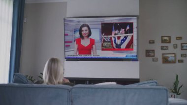 Yetişkin bir kadın oturma odasındaki kanepede dinleniyor ve Amerika Birleşik Devletleri 'ndeki seçimlerle ilgili TV haberleri izliyor. ABD 'de ulusal seçim günü. Televizyon canlı yayında. Vatandaşlık görevi ve vatanseverlik kavramı. Arka plan.