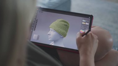 Kadın üç boyutlu tasarım uygulamasında dijital tablet ve stil kullanarak giysiler çizer ve yaratır. Beyaz kadın evdeki kanepede yatarak uzaktan çalışma projesi yapıyor. Yaşam tarzı ve serbest çalışma. Kapat..
