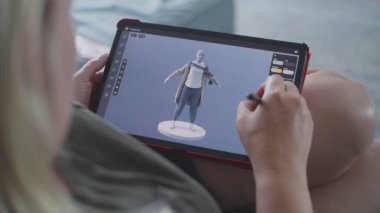 Beyaz kadın tablet bilgisayar ve dijital kalem kullanarak 3D modelleme uygulamasında model oluşturur. Yetişkin bir kadın, evdeki kanepede uzanarak kendi işini yapıyor. Yaşam tarzı ve uzaktan çalışma. Kapat..