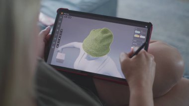 Kadın üç boyutlu tasarım uygulamasında dijital tablet ve stil kullanarak giysiler çizer ve yaratır. Beyaz kadın evdeki kanepede yatarak uzaktan çalışma projesi yapıyor. Yaşam tarzı ve serbest çalışma. Kapat..