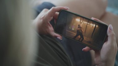 Beyaz kadın koltukta yatarken akıllı telefon kullanarak aksiyon filmi izliyor. Mobil telefon ekranında gerilim filmi gösteriliyor. Beyaz kadın hafta sonları evde dinleniyor. Yaşam tarzı konsepti. Kapat..