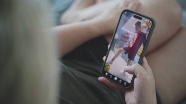 Beyaz bir kadın kanepenin üzerinde yatarken cep telefonu kullanarak uygulamayı kısa videolarla izliyor. Telefon ekranında görüntülenen çeşitli video içerikli akıllı telefon uygulaması. Kapat..