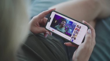 Kanepede yatarken, beyaz bir kadının renk derecelendirme videosunu izlerken cep telefonu kullanmasını kapat. Akıllı telefon ekranında gösterilen renk düzeltmesi hakkında video içeriği içeren video sunucu web sitesi.