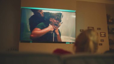 Beyaz kadın geceleri rahat bir oturma odasında kanepede oturur ve büyük bir TV ekranında aksiyon filmi ya da TV şovu izler. Yetişkin bir kadın akşamları evde dinleniyor. Ev sineması. Yaşam tarzı konsepti. El bilgisayarı.