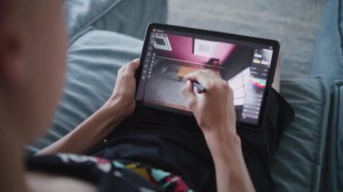 Dijital stili ve tableti olan yetenekli bir genç evde oturup 3 boyutlu bir oda modeli yaratıyor. Yaratıcı tasarımcı 3d modelleme programı kullanarak proje için tasarım çizer. Modern teknolojiler. Kapat..