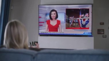 Yetişkin bir kadın oturma odasındaki kanepede dinleniyor ve Amerika Birleşik Devletleri 'ndeki seçimlerle ilgili TV haberleri izliyor. ABD 'de ulusal seçim günü. Televizyon canlı yayında. Vatandaşlık görevi ve vatanseverlik kavramı. Arka plan.