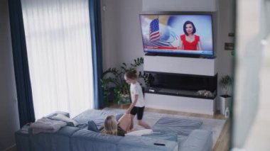 Yetişkin bir kadın modern oturma odasındaki kanepede dinleniyor ve ABD seçimleri hakkında TV haberleri izliyor. Genç kız odaya girer ve kanepeye oturur. Canlı yayın yapan büyük bir TV ekranı. Yüksek açı.