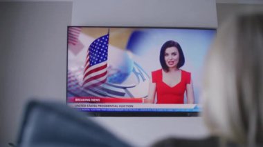 Kadın seçmen modern oturma odasındaki kanepede dinleniyor ve ABD 'de ulusal seçim günüyle ilgili TV haberleri izliyor. Amerika Birleşik Devletleri 'nde seçimler. Televizyon canlı yayında. Vatandaşlık görevi ve vatanseverlik. Kapat..