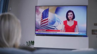 Yetişkin bir kadın rahat bir oturma odasında kanepede dinleniyor ve ABD 'de ulusal seçim günüyle ilgili TV haberleri izliyor. Amerika Birleşik Devletleri 'nde seçimler. Televizyon canlı yayında. Vatandaşlık görevi ve vatanseverlik. Arka plan.