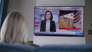 Yetişkin bir kadın oturma odasında kanepede oturur ve Amerika Birleşik Devletleri 'ndeki seçimler hakkında TV haberleri izler. ABD 'de ulusal seçim günü. Televizyon canlı yayında. Vatandaşlık görevi ve vatanseverlik kavramı. Arka plan.
