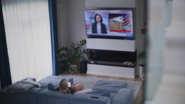 Yetişkin bir kadın oturma odasındaki kanepede dinleniyor, Amerika Birleşik Devletleri 'ndeki seçimlerle ilgili TV haberleri izliyor. ABD 'de ulusal seçim günü. Televizyon canlı yayında. Vatandaşlık görevi ve vatanseverlik kavramı. Yüksek açı.