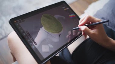 Elinde tablet ve dijital kalemle yetenekli bir çocuk odada oturup 3 boyutlu modeller yaratıyor. Odaklanmış genç, 3D modelleme programı kullanarak oyun karakteri için kıyafet çiziyor. Oyun tasarımı ve geliştirme kavramı.